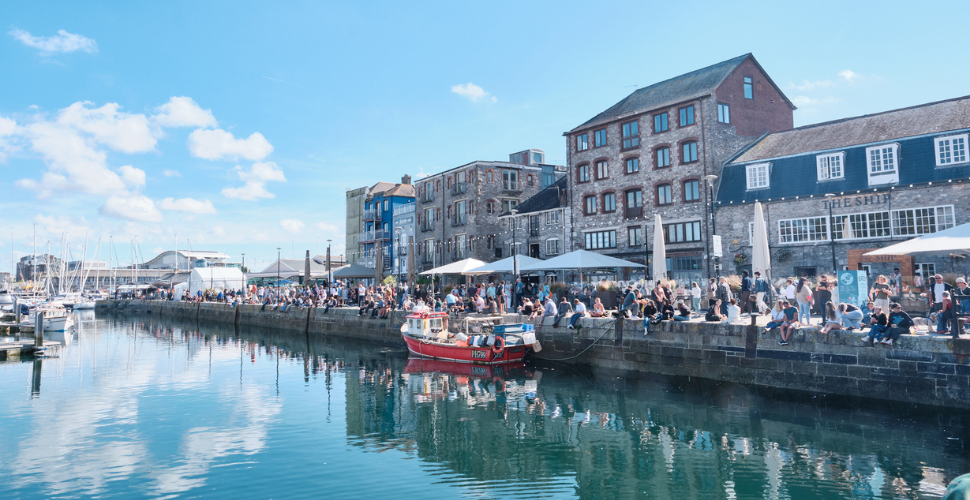 Sunny harbour with a red boat, waterfront cafés, and crowds along the quay
